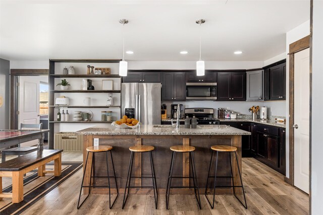 1521 Cheery Dr, Belgrade, MT 59714 - kitchen with appliances with stainless steel finishes, open shelves, a center island with sink, and light stone counters