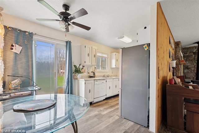 kitchen featuring white dishwasher, freestanding refrigerator, a ceiling fan, and white cabinetry