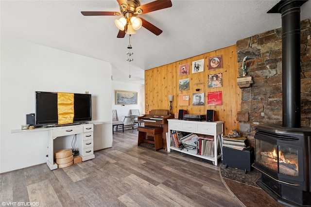 office space featuring ceiling fan, wood walls, wood finished floors, and a wood stove