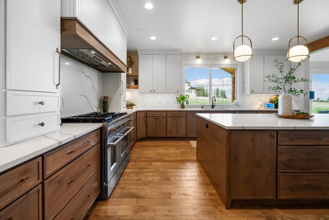 kitchen with wall chimney range hood, a sink, range with two ovens, white cabinetry, and light wood-type flooring