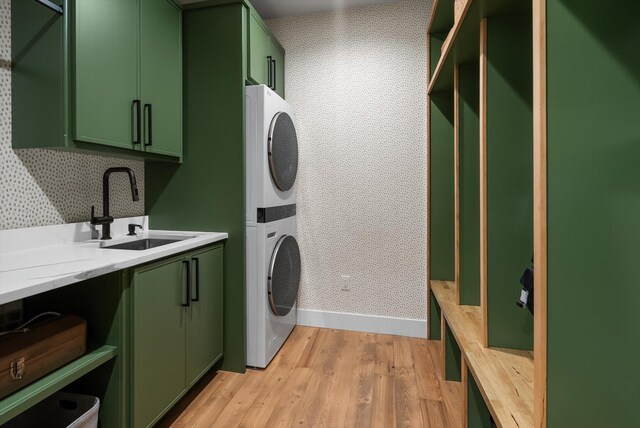 clothes washing area featuring stacked washer / dryer, baseboards, light wood-type flooring, a sink, and cabinet space