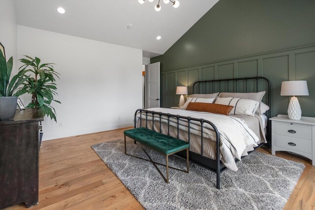bedroom featuring light wood-style flooring, a decorative wall, and high vaulted ceiling