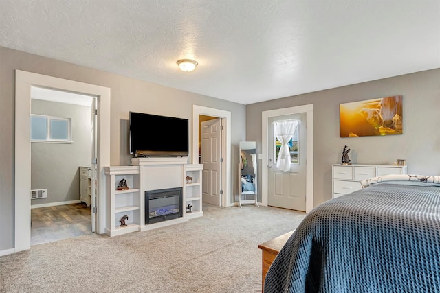 bedroom featuring carpet floors, visible vents, a glass covered fireplace, baseboards, and a textured ceiling