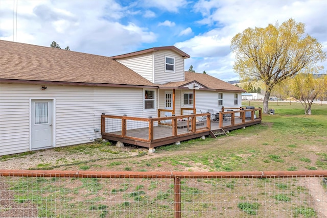 back of house with a lawn, a wooden deck, and roof with shingles