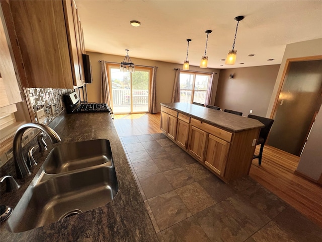 kitchen with brown cabinets, dark countertops, a sink, backsplash, and pendant lighting