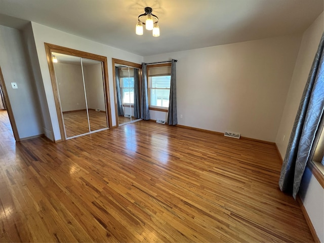 unfurnished bedroom with baseboards, multiple closets, light wood-style flooring, and visible vents