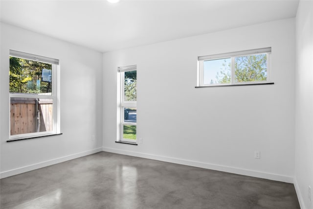 empty room with finished concrete flooring, baseboards, and a wealth of natural light