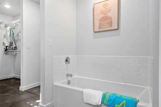 full bathroom featuring baseboards, finished concrete floors, and a bath