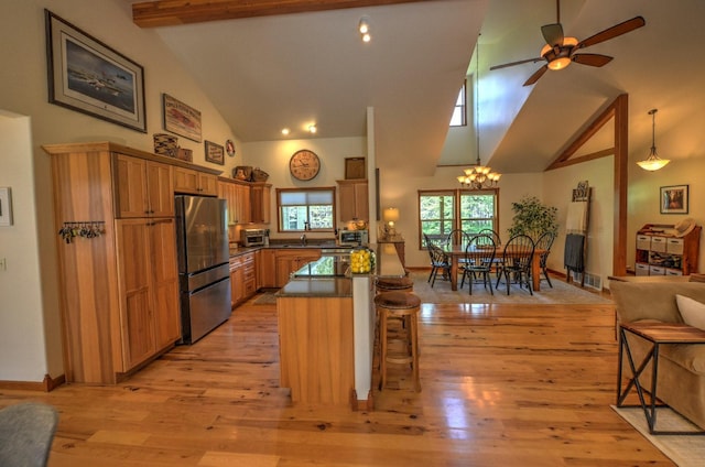 kitchen with a breakfast bar area, high vaulted ceiling, ceiling fan with notable chandelier, freestanding refrigerator, and light wood-type flooring