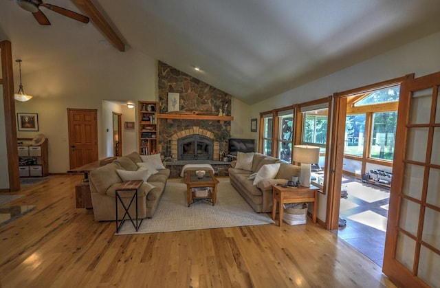 living area featuring beamed ceiling, high vaulted ceiling, a stone fireplace, and light wood finished floors