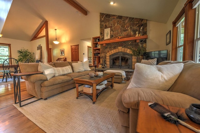 living room with a stone fireplace, light wood-style flooring, high vaulted ceiling, and beamed ceiling