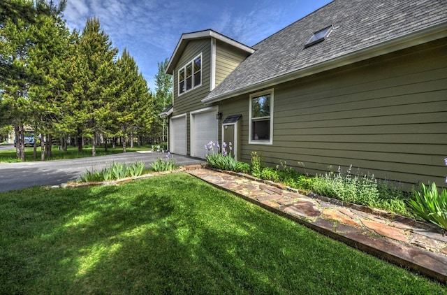 view of side of home featuring a shingled roof, an attached garage, a yard, and aphalt driveway