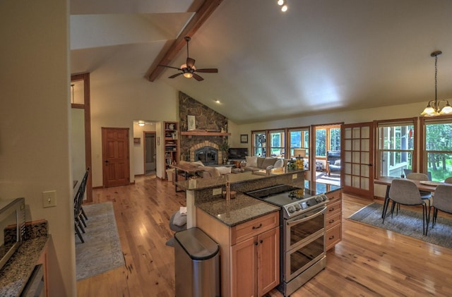 kitchen with light wood-type flooring, ceiling fan with notable chandelier, a fireplace, and range with two ovens