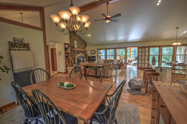 dining area with beam ceiling, light wood finished floors, high vaulted ceiling, a stone fireplace, and ceiling fan with notable chandelier