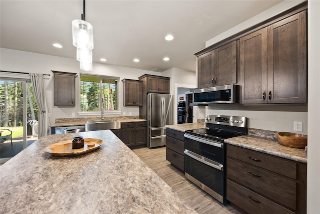 kitchen with dark brown cabinetry, a sink, light wood-style flooring, stainless steel appliances, and decorative light fixtures