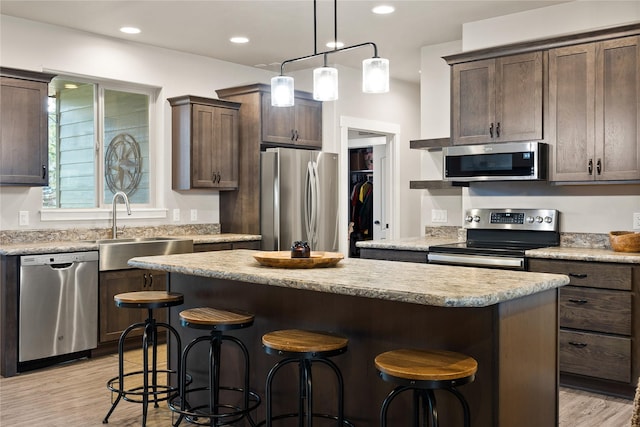 kitchen featuring dark brown cabinets, appliances with stainless steel finishes, a breakfast bar, a sink, and a center island
