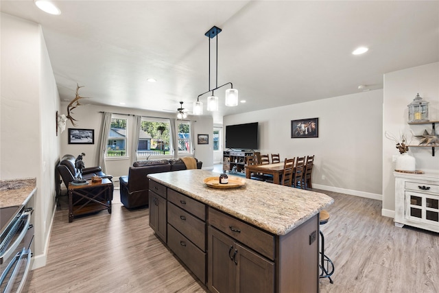 kitchen featuring stainless steel range with electric stovetop, open floor plan, a breakfast bar area, a center island, and light wood-style flooring