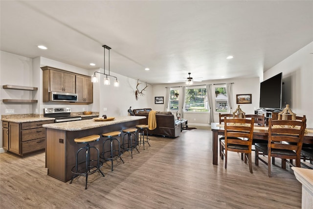 kitchen with open shelves, a breakfast bar, light wood-style floors, open floor plan, and appliances with stainless steel finishes