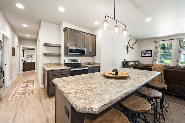 kitchen featuring dark brown cabinetry, a breakfast bar, open floor plan, light wood-style flooring, and appliances with stainless steel finishes