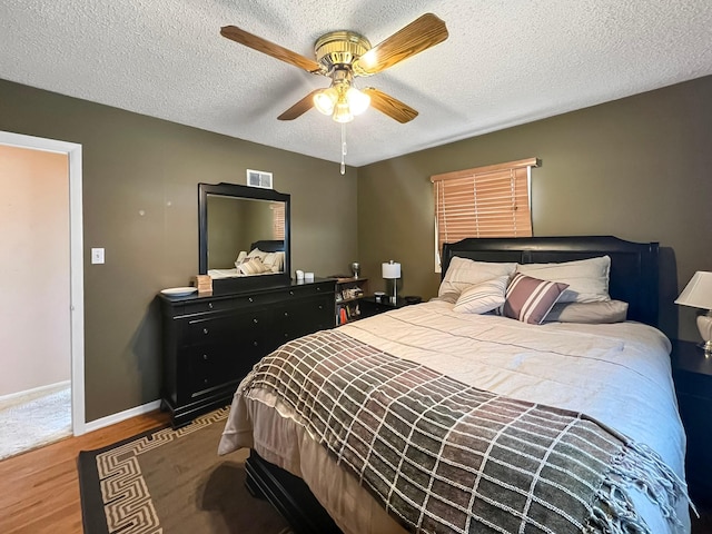bedroom with a textured ceiling, baseboards, visible vents, and wood finished floors