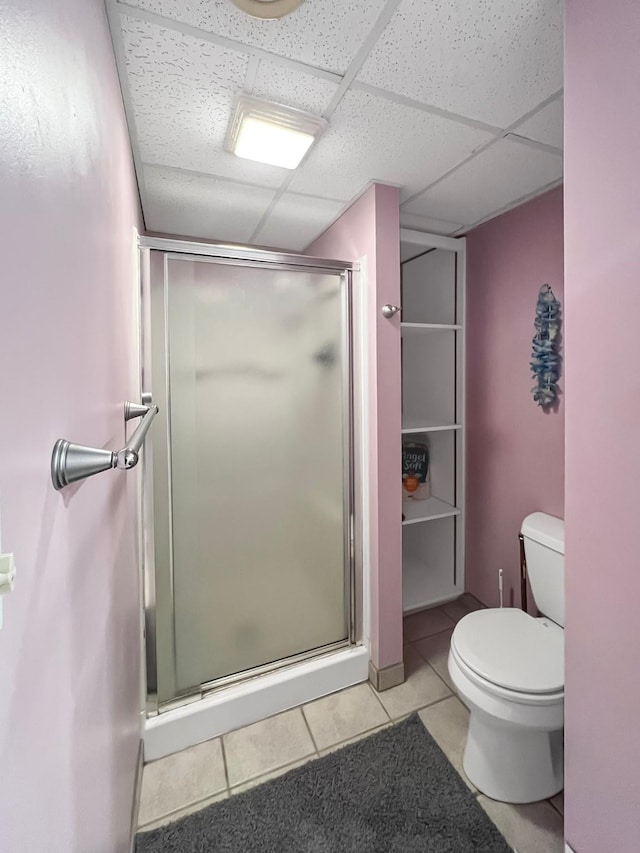 bathroom with tile patterned flooring, a drop ceiling, a stall shower, and toilet