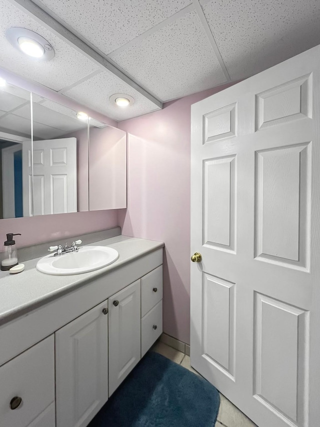 bathroom with tile patterned flooring, a drop ceiling, and vanity