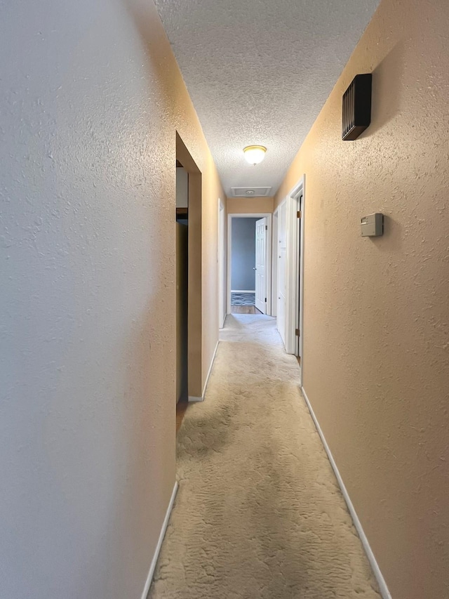 corridor with a textured ceiling, a textured wall, light carpet, and baseboards