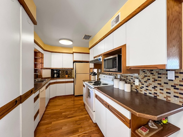 kitchen featuring a sink, dark countertops, under cabinet range hood, and white appliances