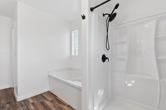 bathroom featuring baseboards, walk in shower, wood finished floors, and a garden tub