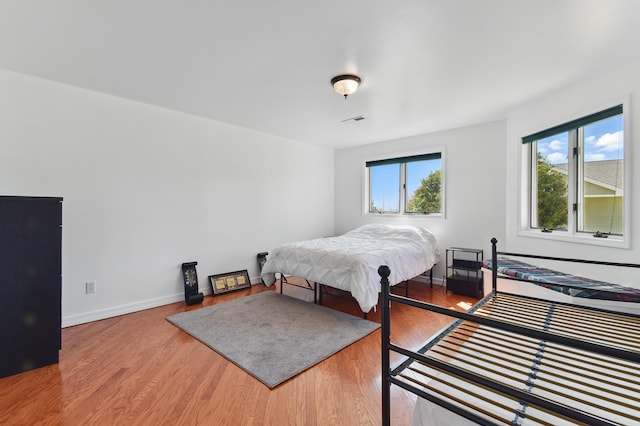 bedroom with baseboards, visible vents, multiple windows, and wood finished floors