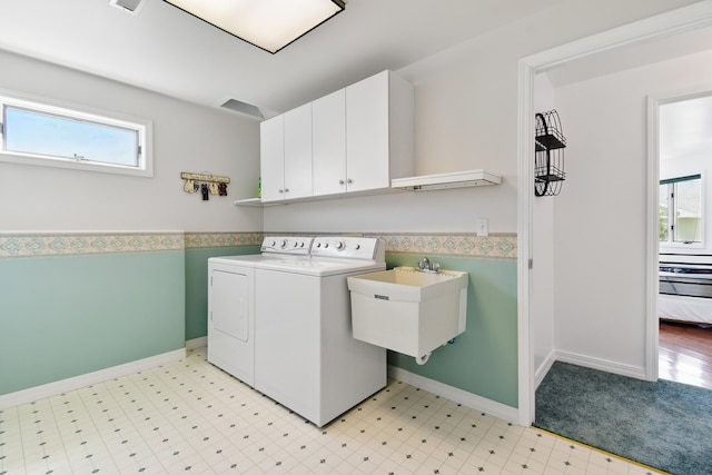 clothes washing area with independent washer and dryer, cabinet space, a sink, baseboards, and light floors
