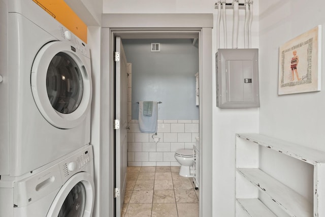 bathroom with electric panel, stacked washer / dryer, visible vents, tile walls, and toilet