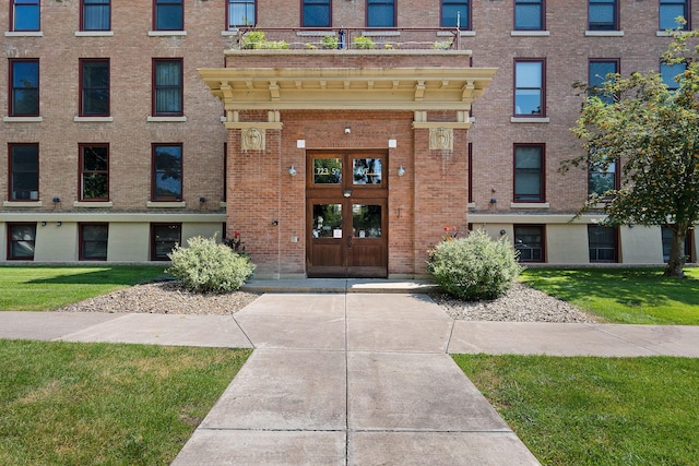 entrance to property featuring a lawn, brick siding, and french doors