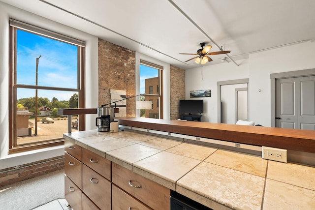 kitchen with ceiling fan, tile counters, brick wall, and open floor plan