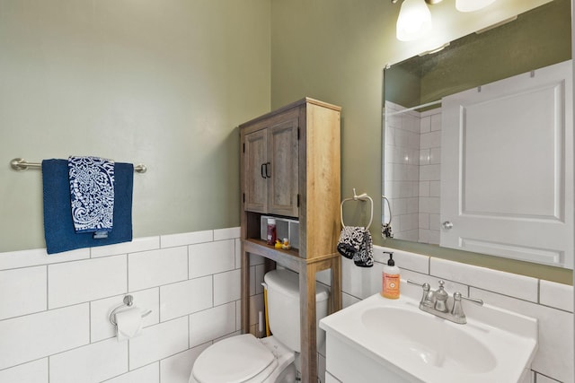 bathroom with vanity, wainscoting, a shower, toilet, and tile walls