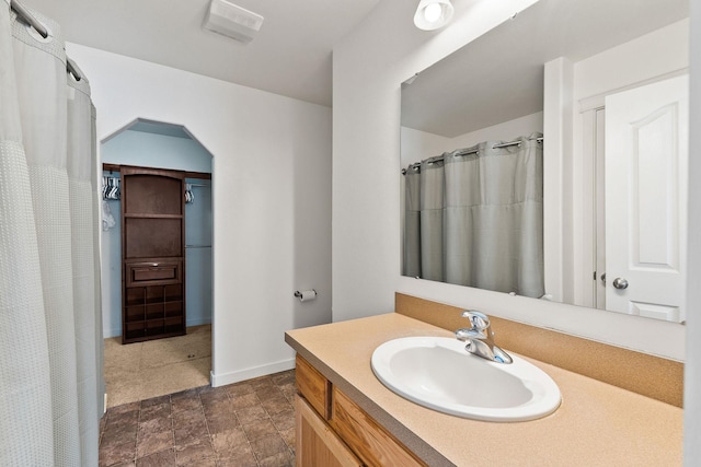 full bath featuring vanity, visible vents, curtained shower, baseboards, and stone finish floor