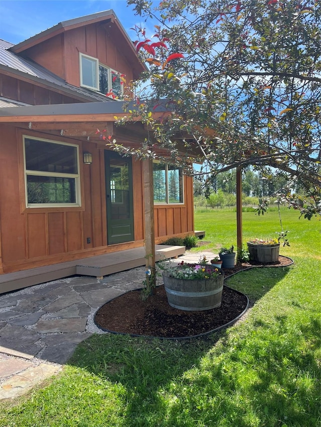 view of exterior entry with board and batten siding, a yard, and metal roof