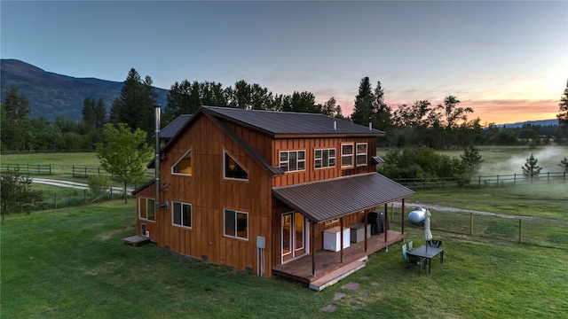 back of house at dusk featuring board and batten siding, a yard, fence, and metal roof