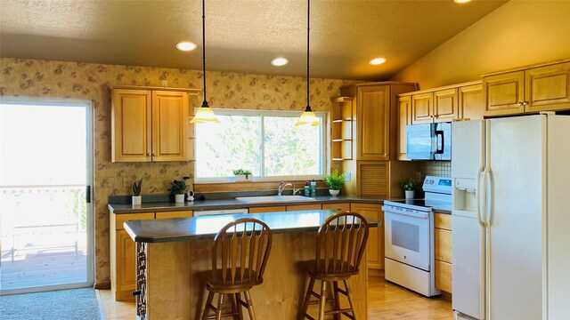 kitchen with dark countertops, a sink, white appliances, a kitchen breakfast bar, and recessed lighting