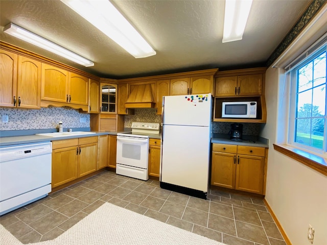 kitchen featuring a sink, backsplash, custom range hood, and white appliances