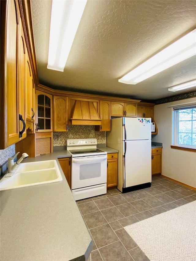 kitchen with a sink, brown cabinetry, custom range hood, and white appliances