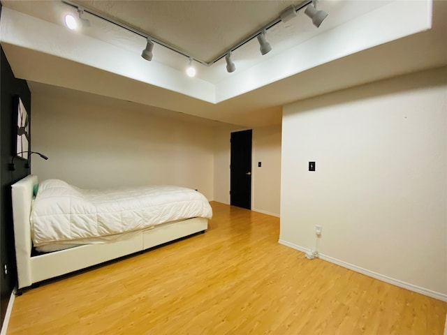 bedroom with baseboards, rail lighting, and wood finished floors