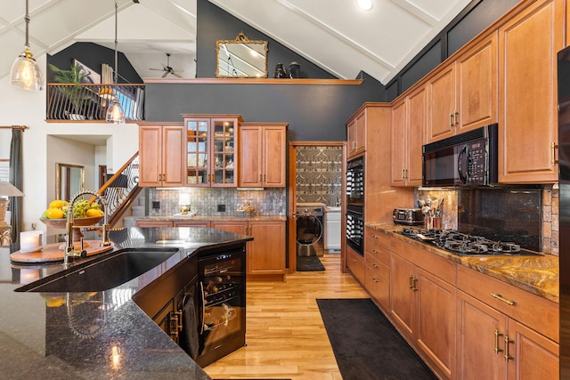 kitchen with decorative backsplash, washer / dryer, light wood-type flooring, a sink, and black appliances