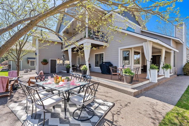 rear view of house with outdoor dining space, a chimney, a patio area, and a balcony