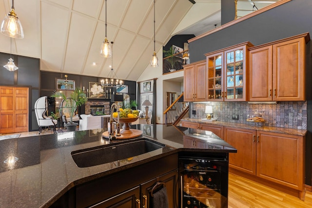 kitchen with decorative backsplash, wine cooler, lofted ceiling, a stone fireplace, and a sink