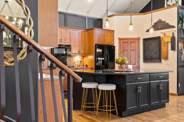 kitchen featuring dark countertops, a breakfast bar, light wood finished floors, high vaulted ceiling, and black appliances