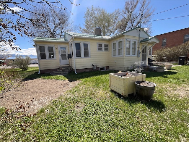rear view of house featuring a lawn, metal roof, a chimney, and entry steps