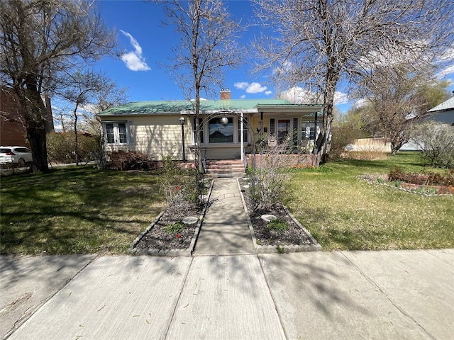 view of front facade featuring covered porch, a chimney, metal roof, and a front lawn