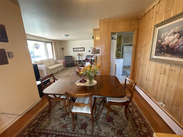 dining area featuring baseboards, a baseboard radiator, wood finished floors, and wooden walls