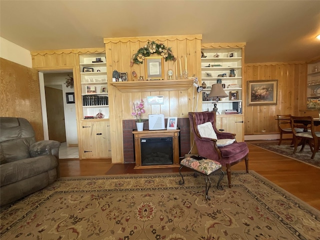 living room with wooden walls, built in shelves, and wood finished floors